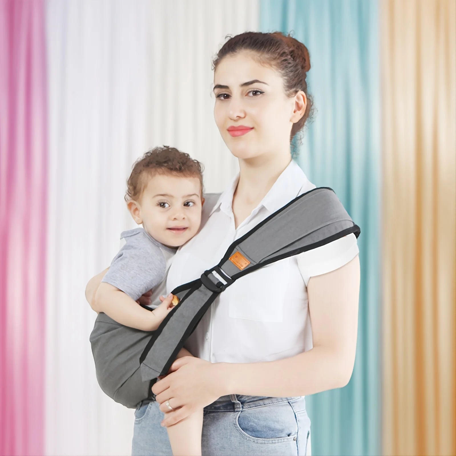 La photo montre une maman avec son enfant en bandoulière dans le porte bébé.
