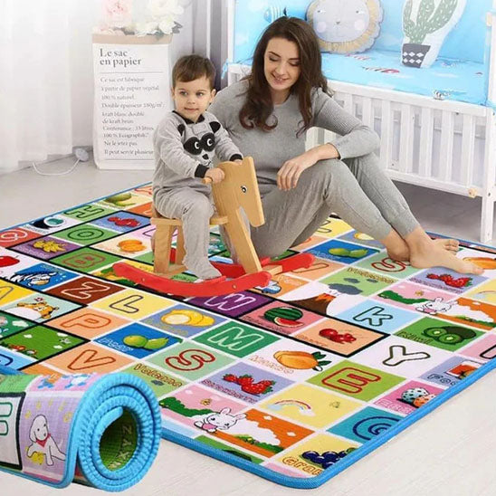 La photo montre une maman et son enfant assis sur un tapis de jeu en mousse tout décoré de chiffres, lettres ainsi que différents animaux.