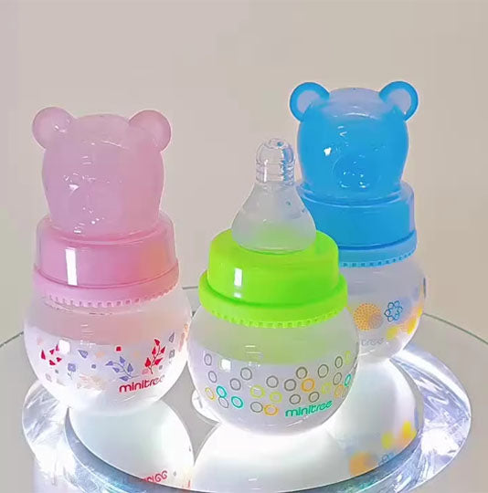 Baby bottles, specifically wide-bore PP bottles with bear-shaped caps, available in pink, green, and blue colors.