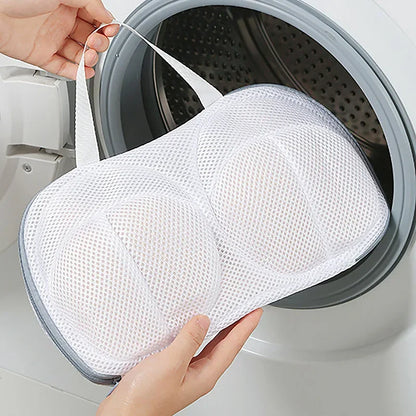 La photo montre une femme qui dépose un filet de lavage rempli de soutiens-gorge dans la machine à laver.